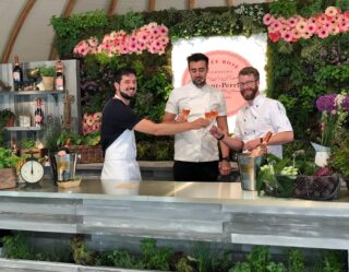 Three men toasting at an outdoor bar with flowers