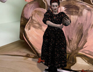 Person in black dress standing before floral artwork
