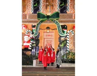 Carolers in red dresses at decorated holiday storefront