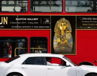 White car parked in front of red London bus